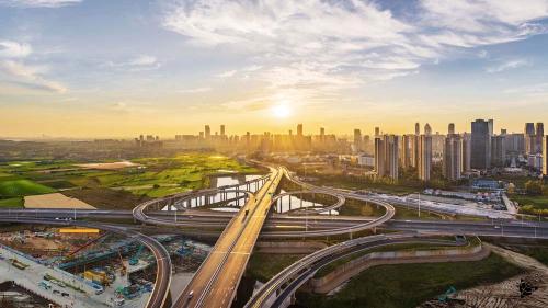 Aerial view of cityscape with roads and tall buildings, with sun rising in the horizon.